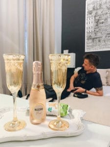 Stephen is in our hotel in Naples, Italy with a bottle and glasses of sparkling wine. Travel planning to find the best perks is half of the fun!