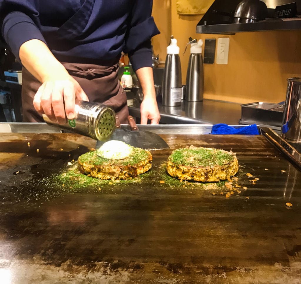 a chef prepares okonomiyaki on a grill in Japan