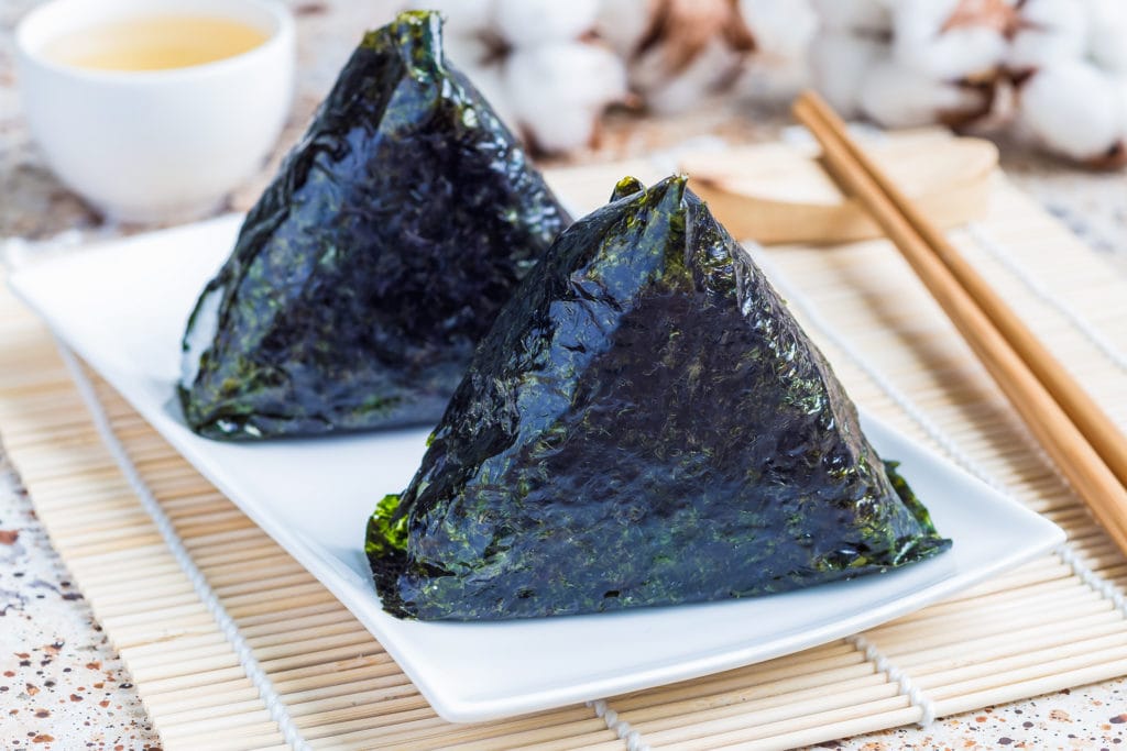 seaweed-wrapped triangles of onigiri on a plate with chop sticks