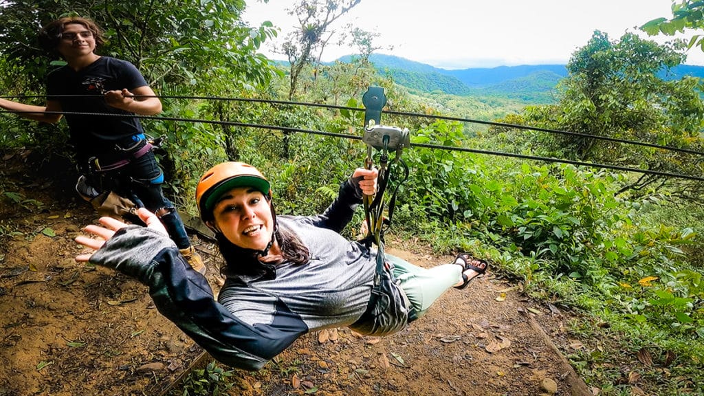 Woman waving to camera as she zip lines away in the cloud forest. Mindo Nambillo Ecological Reserve. Zip lining is one of the best things To Do and See In Mindo, Ecuador